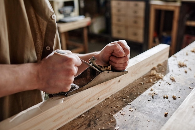 Medium closeup of unrecognizable carpenter working in workshop using hand plane to shape and smooth