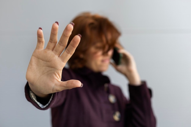 Medium closeup of a young Latin American woman 22 with red hair she doesn't want to be photographed while talking on her cell phone wearing a purple coat Focus on her hand Concept Technology