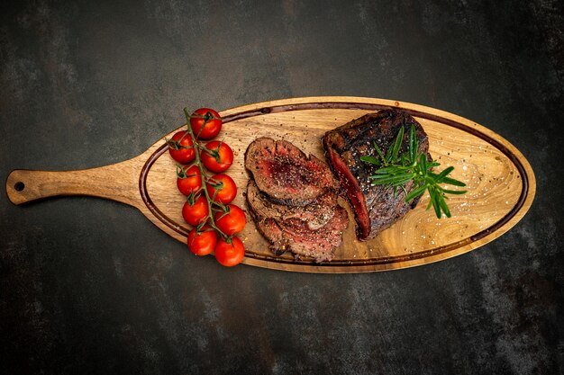 Medium cooked steak served with red cherries on a wooden board