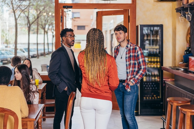 Medium full shot of 3 people of different ethnicities conversing inside a bar