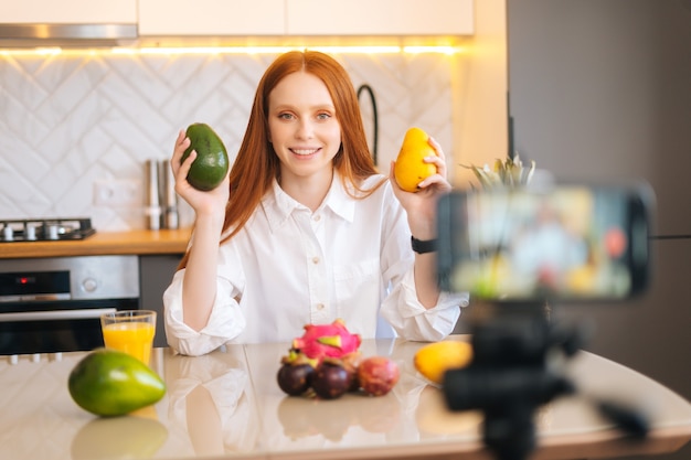 Medium shot of female vlogger shooting culinary show speaking about exotic fruits looking at camera