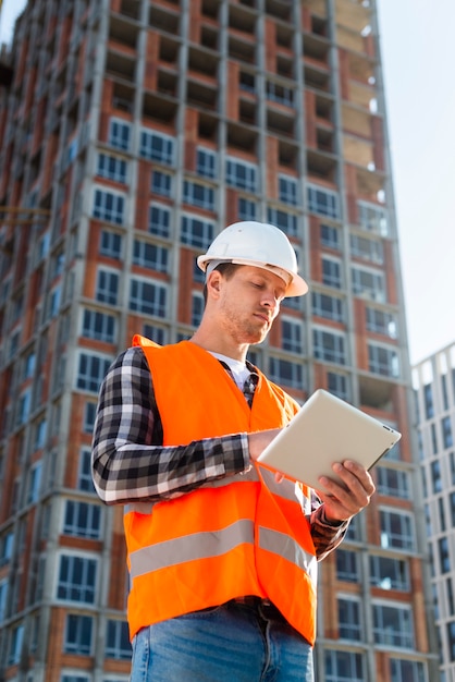 Medium shot low angle view construction engineer looking at tablet