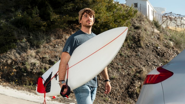 Medium shot young man holding surfboard