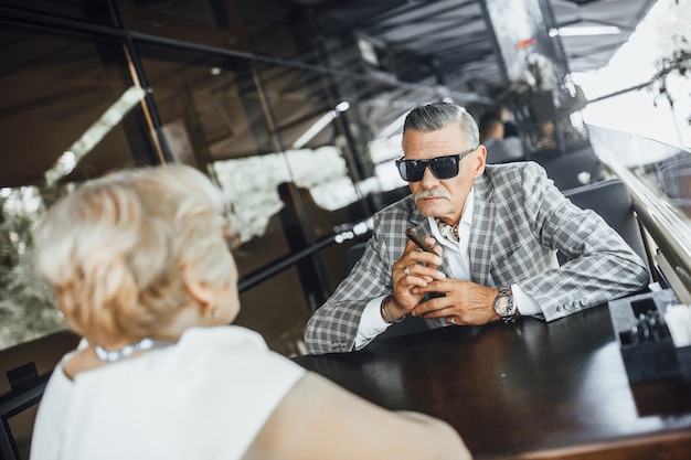 Meet two seniors couplein modern restaurant ,man smoking his cigarette.