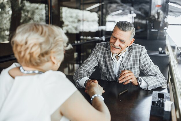 Meet of two seniors in love, they are sitting at summer terrace and looking each other