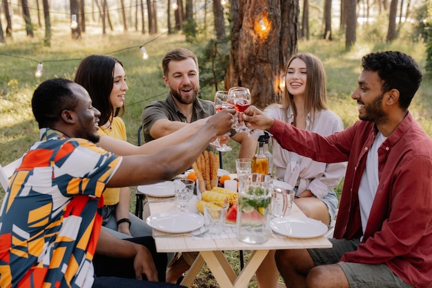 Meeting of multiracial group of friends eating dinner and drinking wine during party in the forest