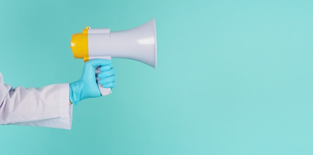 Megaphone in hand.Man wear doctor gown and blue medical glove on mint green or Tiffany Blue  background. Studio shooting.