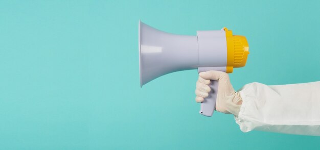 Megaphone in woman's hands on green or Tiffany Blue background.
.woman wear ppe suit and white medical glove or latex glove.