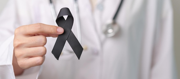 Melanoma and skin cancer Vaccine injury awareness month and rest in peace concepts doctor holding black Ribbon