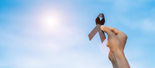 Photo melanoma and skin cancer, vaccine injury awareness month and rest in peace concepts. man holding black ribbon on sky background