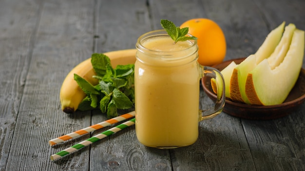 Melon smoothie mug with mint leaves, melon slices and cocktail tubes on a wooden table.