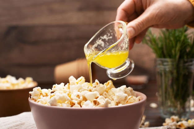 Melted butter being poured on popcorn in clay bowl on kitchen table