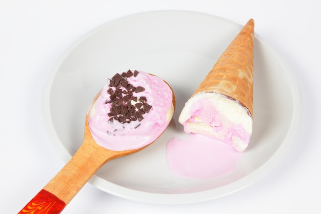 Melted ice cream with waffle cone and wooden spoon on white plate isolated on white background Pink ice cream on a white plate closeup