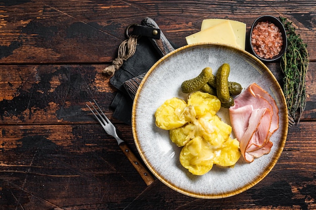 Melted Raclette Swiss cheese with boiled potato and ham Wooden background Top view Copy space