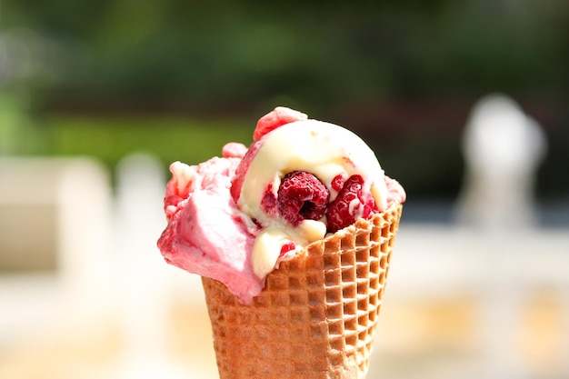 Melting raspberry ice cream in a waffle cone in a womans hand against blurred background summer mood