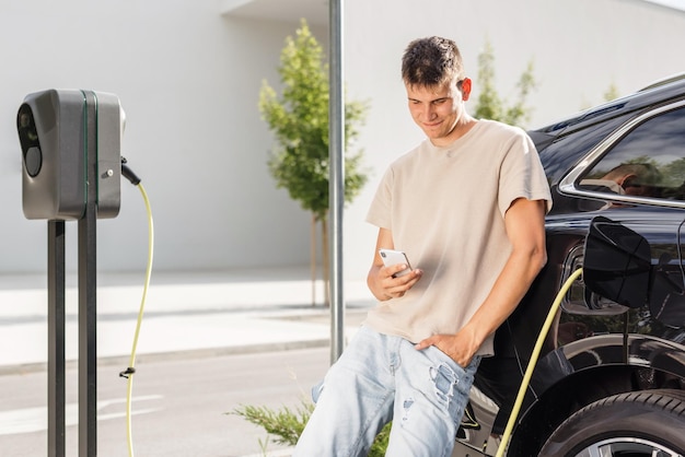 Men charging electric car in city and adjusting ev charging app on smartphone