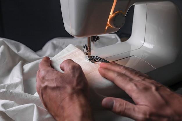 Men hand at sewing machine during working with organic natural cotton cloth closeup