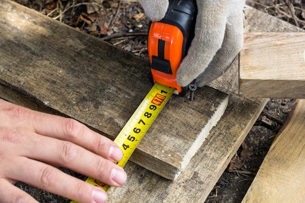 Men hands measuring a wooden board with a roulette on construction site