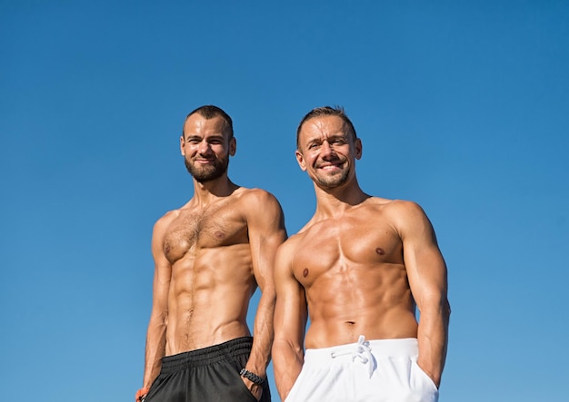 Men muscular body posing confidently with hands in pockets. Sport and bodycare. Muscular masculine guys look confident. Men sexy muscular bare torso stand outdoor. Sportsmen muscular belly posing.