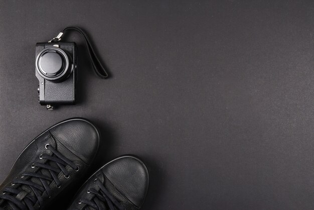 Men's black leather shoes and a black camera on a black wall. Copy space.