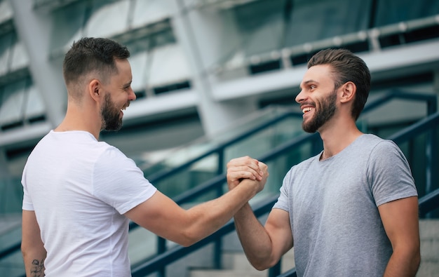 Men's friendly handshake. Two young bearded handsome friends in casual t-shirts are posing together