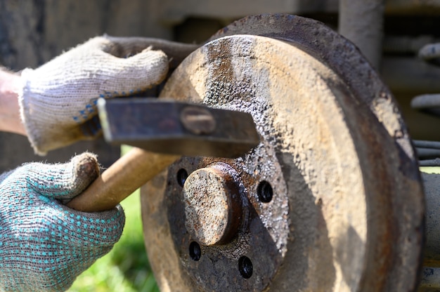 Men's gloved hands repair of car drum brake himself. disassembles a jammed disk with a hammer. repair of broken car drum brake disassembled outdoor