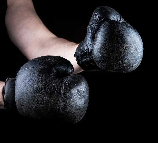 Men's hands are wearing old leather black boxing gloves