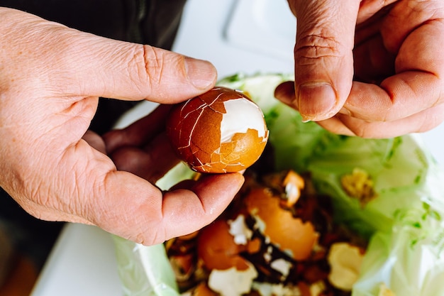 Men's hands clean shell from boiled eggs in bucket of biological food waste