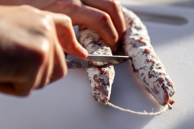 Men's hands cut with knife french cured sausage with white mold on cutting board closeup