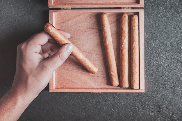 men's hands take a cigar out of the box on a dark table