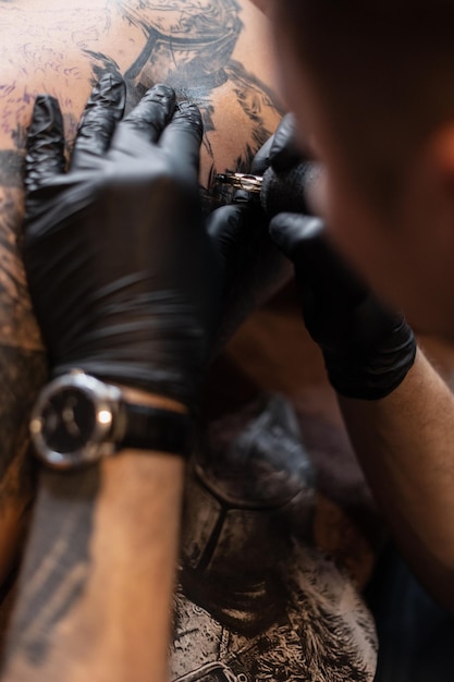 Men's hands of a tattoo artist in black gloves with a tattoo machine gets a tattoo on the skin, close-up