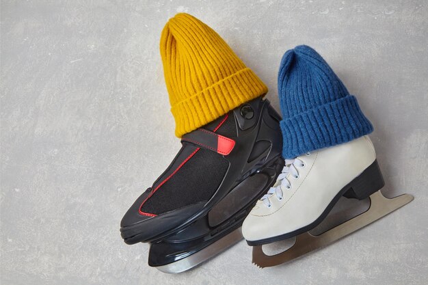 Men's and women's skates in knitted blue and yellow winter hats on a gray concrete background