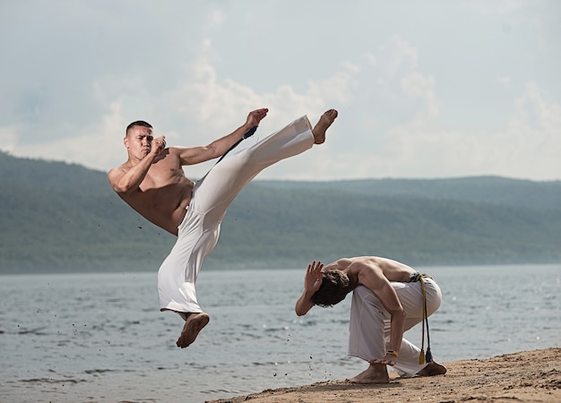 Men train capoeira on the beach 