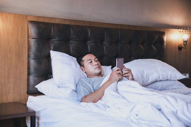 Men using smartphone while lying on the bed using a blanket