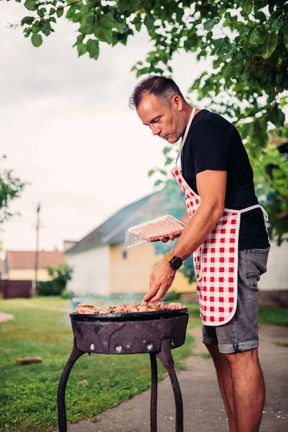 Men wearing apron barbecuing meat in the backyard