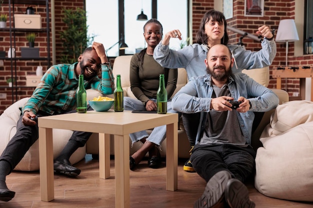 Men and women laughing while they play strategy video games, using controller and tv console to have fun together. Young people enjoying leisure activity with beer bottles and gaming teamwork.