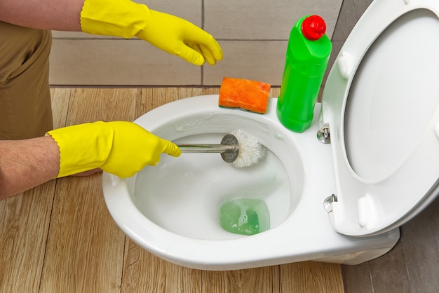 Men in yellow gloves cleaning toilet bowl home cleaning concept