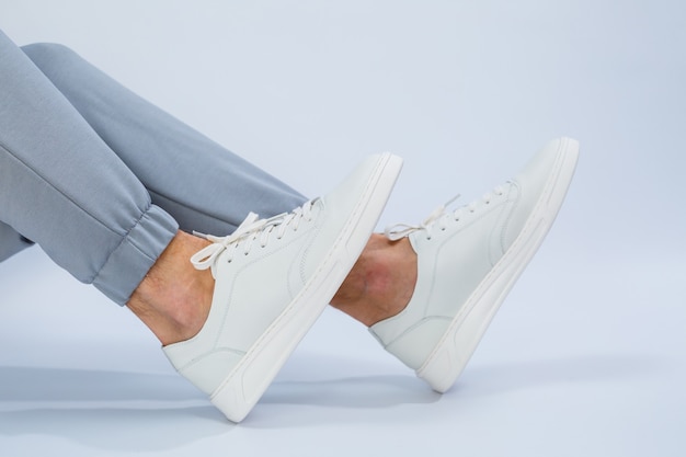 Mens feet in white everyday sneakers made of natural leather on lacing