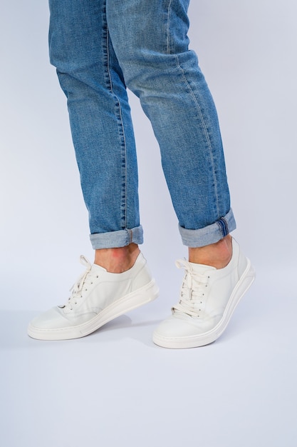 Mens feet in white everyday sneakers made of natural leather on lacing