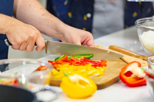 Mens hands cut red and yellow pepper on the wooden board close up