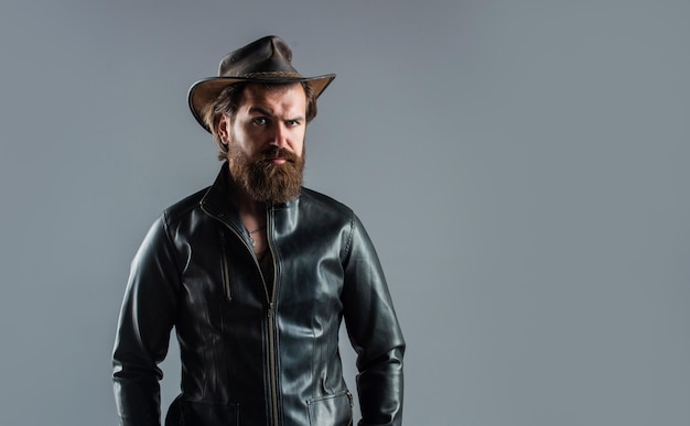 Mens western wardrobe fashionable man dressed in leather jacket west fashion model handsome man in cowboy hat serious bearded biker stylish mature man looking modern