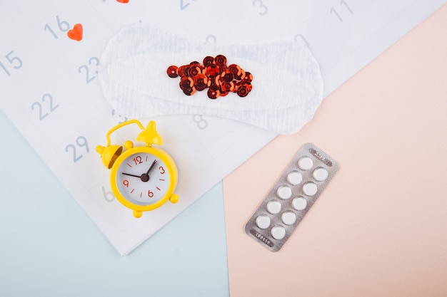 Menstrual calendar with pads, alarm clock and contraceptive pills. Menstruation period concept. Pain reliever for menstrual pain.