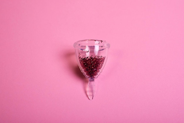 Menstrual cup filled by red sparkles against pink background