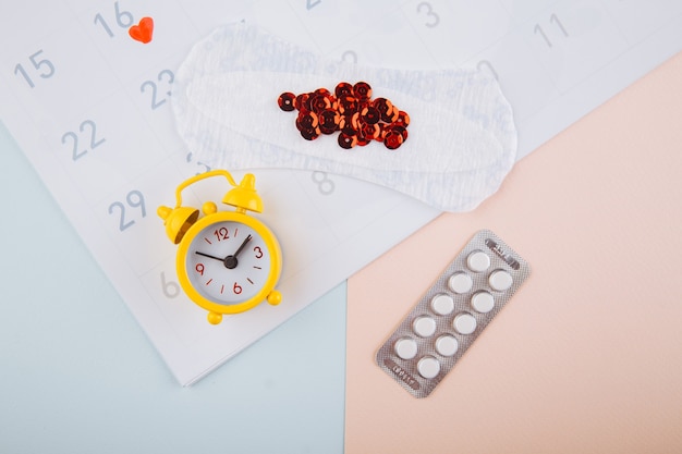 Menstruation calendar with yellow alarm, cotton tampon and contraceptive pills on pink background. Woman critical days, woman hygiene protection concept.