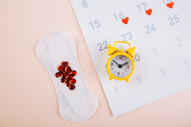 Menstruation calendar with yellow alarm and daily sanitary pads on pink background. Woman critical days, woman hygiene protection concept.