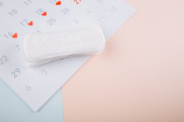 Menstruation woman hygiene concept. Minimal flat lay menstrual pad and calendar on a blue pink background.