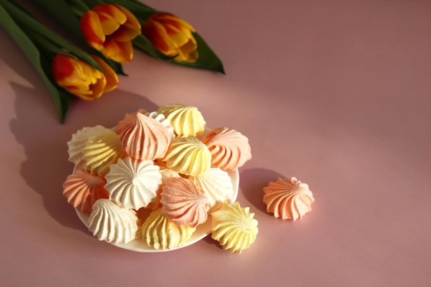 Meringue pink white yellow on a saucer on a pink background with variegated tulips