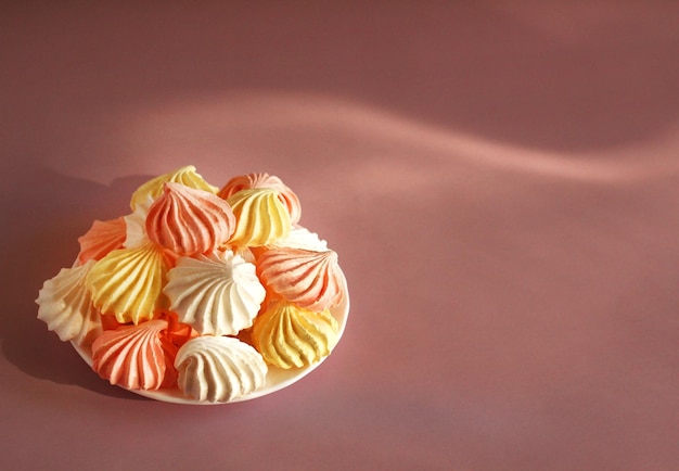 Meringue pink white yellow on a saucer on a pink background