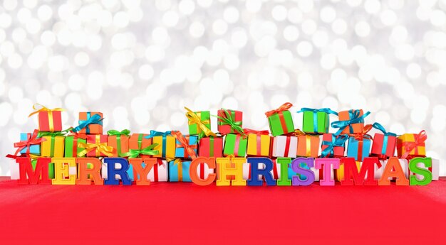 Merry christmas colorful text on the background of varicolored gifts on a bokeh background