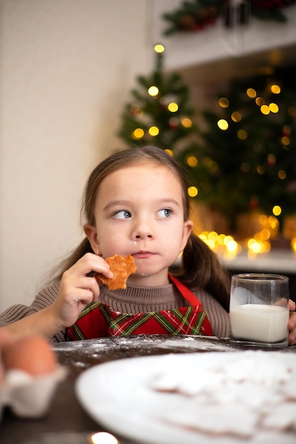 Merry Christmas A funny sweet girl in a cozy decorated kitchen baked Christmas cookies and eats them Lifestyle Warm tones